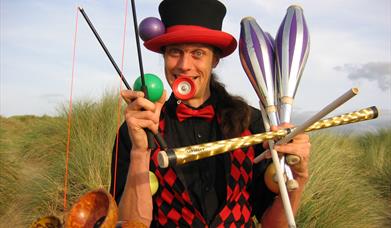 A circus performer holding a array of equipment including juggling batons and diablos.