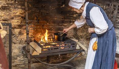 A woman dressed in Tudor clothing standing over an open fire