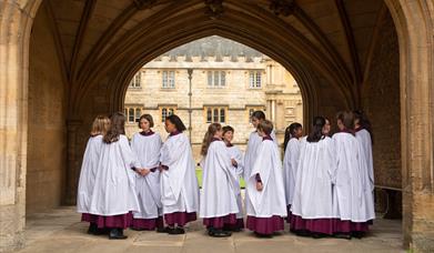 The Girl Choristers talk in robes under an ancient arch