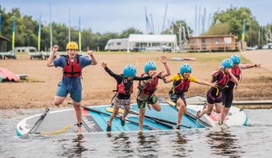 Young people jumping from a mega stand up paddleboard into a lake