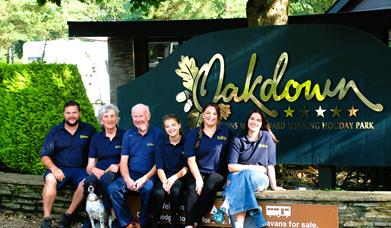 family of owner sitting outside the sign @Oakdown Touring and Holiday Caravan Park